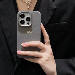 May include: A grey leather phone case with a camera lens cutout and the initials "KS" in gold lettering.