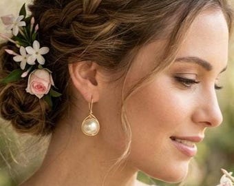 May include: A person with a braided hairstyle adorned with small white and pink flowers, wearing a gold drop earring with a round pearl and a white lace sleeveless top, holding a bouquet of white and pink roses and small white flowers.