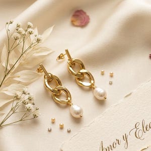 May include: A pair of gold-toned drop earrings featuring a polished chain link design. Each earring is finished with a single white, irregular-shaped freshwater pearl dangling from the bottom of the metal links. The earrings include post-style backs.