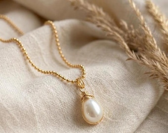 May include: A gold-toned necklace featuring a delicate ball chain and a teardrop-shaped white pearl pendant. The pearl is secured at the top with a decorative gold wire wrapping, creating a simple and elegant piece of jewelry with a polished finish.