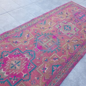 May include: A pink and teal vintage rug with a geometric pattern. The rug has a faded look and is made of wool.