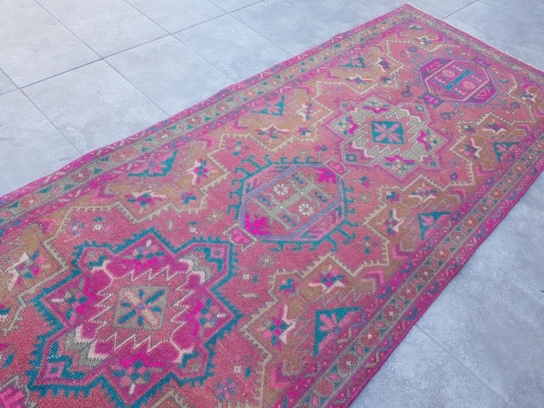 May include: A pink and teal vintage rug with a geometric pattern. The rug has a faded look and is made of wool.