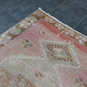 May include: A vintage pink and brown rug with a geometric pattern. The rug has a frayed edge and is made of wool.