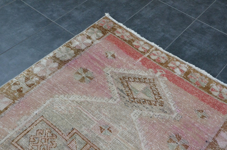 May include: A vintage pink and brown rug with a geometric pattern. The rug has a frayed edge and is made of wool.