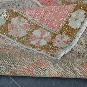 May include: A vintage rug with a faded floral pattern in shades of brown, pink, and white. The rug has a frayed edge and a worn texture.