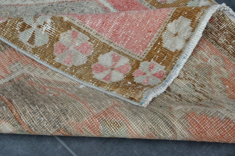 May include: A vintage rug with a faded floral pattern in shades of brown, pink, and white. The rug has a frayed edge and a worn texture.