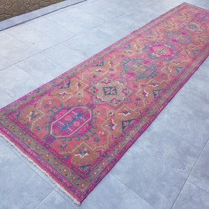 May include: A pink and brown patterned runner rug with a fringed edge. The rug has a traditional design with geometric shapes and floral motifs.