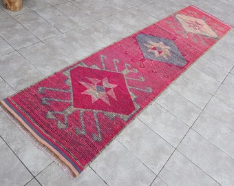 May include: A long, narrow pink and gray rug with a geometric pattern. The rug has a fringed edge and is made of woven fabric.