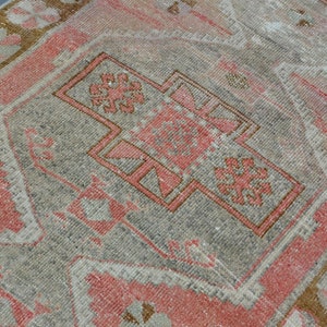May include: A vintage Turkish rug with a faded pink and gray color scheme. The rug features a central medallion with intricate geometric patterns and a border with floral motifs.