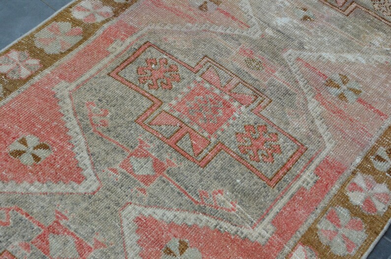 May include: A vintage Turkish rug with a faded pink and gray color scheme. The rug features a central medallion with intricate geometric patterns and a border with floral motifs.