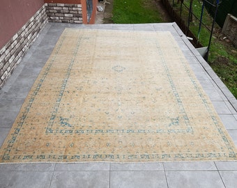 May include: A beige rug with a blue and white floral pattern. The rug has a fringed edge and is made of a soft, woven material.