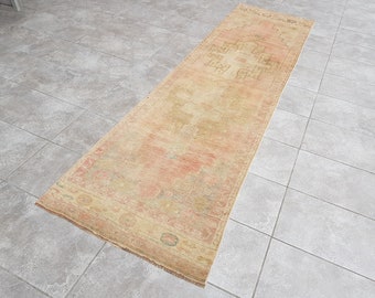 May include: A rectangular, vintage-style rug with a faded, distressed appearance. The rug features a central design in shades of peach and beige, with a border in similar tones. The rug is placed on a tiled floor.