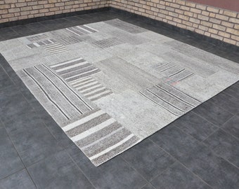 May include: A gray and white patterned rug with a patchwork design. The rug is made of woven fibers and has a subtle texture.