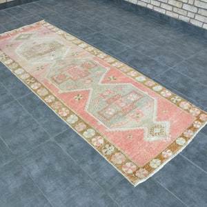 May include: A pink and beige runner rug with a traditional floral pattern. The rug has a faded, vintage look and is perfect for adding a touch of bohemian style to any room.