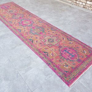 May include: A pink and gold patterned runner rug with a fringed edge. The rug has a traditional design with intricate details.