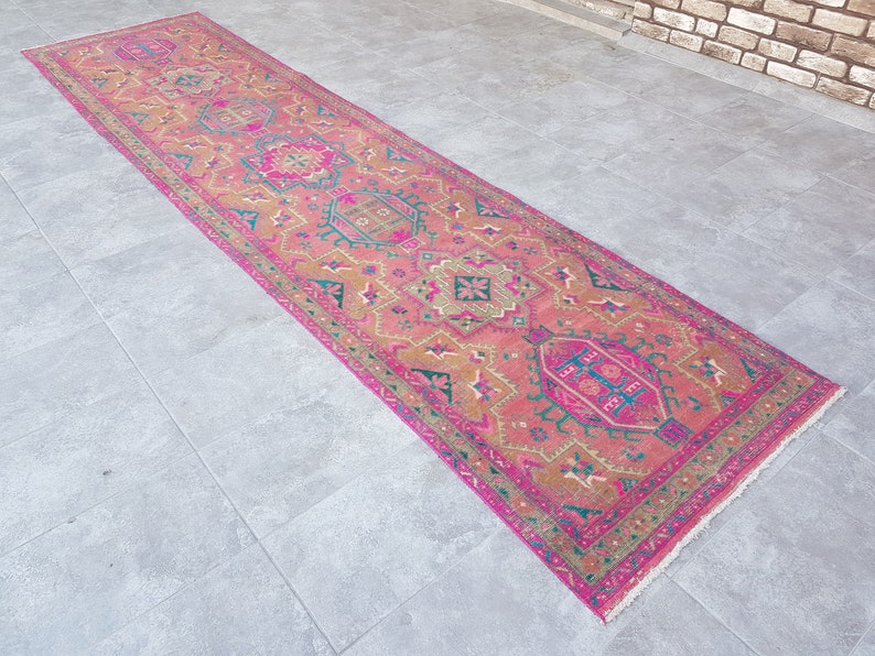 May include: A pink and gold patterned runner rug with a fringed edge. The rug has a traditional design with intricate details.