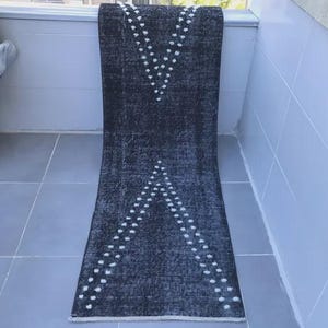 Peut inclure: Un tapis de couloir gris foncé à l'aspect vieilli. Le tapis présente un motif répétitif de points blancs disposés en chevrons. Le tapis est rectangulaire et semble être fait d'une matière tissée. Mesure environ 200 cm de long.