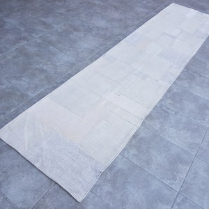 Puede incluir: Un camino de mesa blanco de patchwork con forma rectangular. La alfombra está hecha de diferentes piezas de tela blanca cosidas juntas.