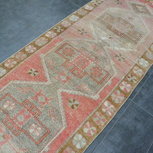 May include: A vintage runner rug with a faded pink and beige color scheme. The rug features a traditional geometric pattern with a central medallion.