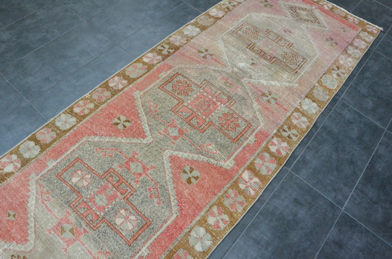 May include: A vintage runner rug with a faded pink and beige color scheme. The rug features a traditional geometric pattern with a central medallion.
