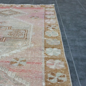 May include: A vintage rug with a faded pink and brown floral pattern. The rug has a worn, distressed look and is perfect for adding a touch of bohemian style to any room.