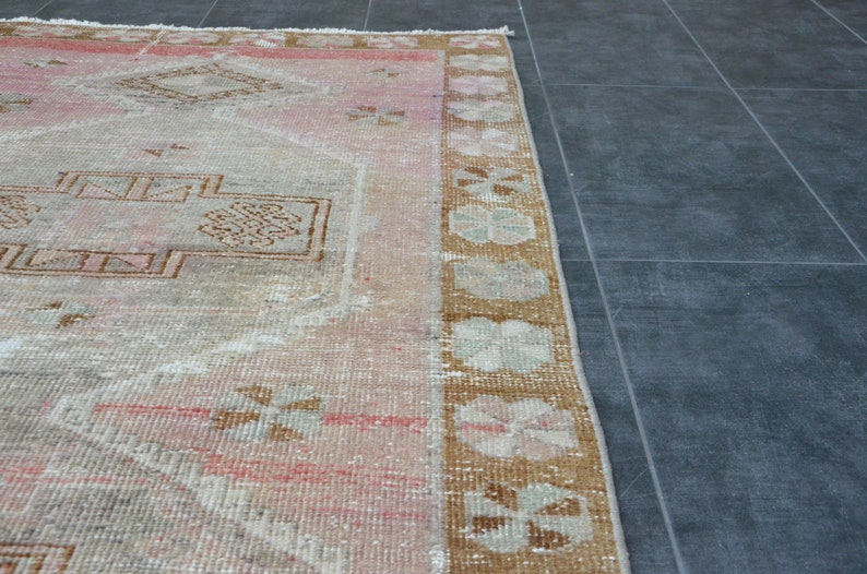 May include: A vintage rug with a faded pink and brown floral pattern. The rug has a worn, distressed look and is perfect for adding a touch of bohemian style to any room.