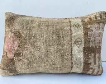 May include: Rectangular beige pillow with a woven texture. The pillow features a faded design with brown and pink accents. The pillow's design is reminiscent of a vintage rug.