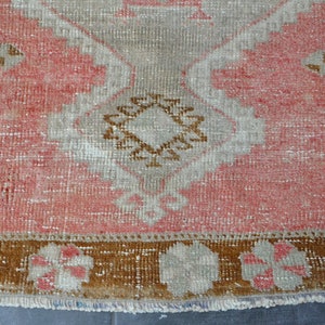 May include: A vintage rug with a pink background and a brown and white geometric pattern. The rug has a fringe border.