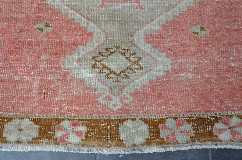 May include: A vintage rug with a pink background and a brown and white geometric pattern. The rug has a fringe border.