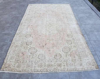 May include: A vintage rug with a light pink background and a beige floral pattern. The rug has a fringed edge.
