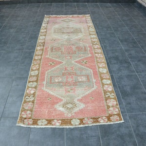 May include: A long, rectangular rug with a pink, beige, and brown geometric pattern. The rug has a faded, vintage look and is perfect for adding a touch of bohemian style to any room.