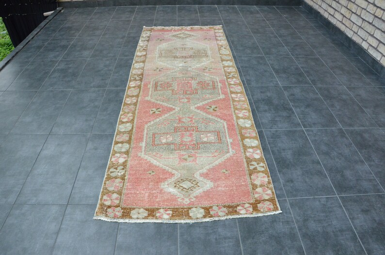May include: A long, rectangular rug with a pink, beige, and brown geometric pattern. The rug has a faded, vintage look and is perfect for adding a touch of bohemian style to any room.
