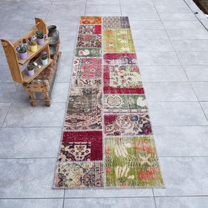 Puede incluir: Una alfombra larga y rectangular de patchwork con una variedad de colores y patrones, incluyendo rojo, verde y beige. La alfombra está compuesta por cuadrados y rectángulos más pequeños de diferentes telas, creando un aspecto único y ecléctico.