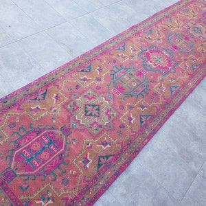 May include: A pink and brown patterned runner rug with intricate geometric designs. The rug has a fringed edge and is made of a soft, woven material.