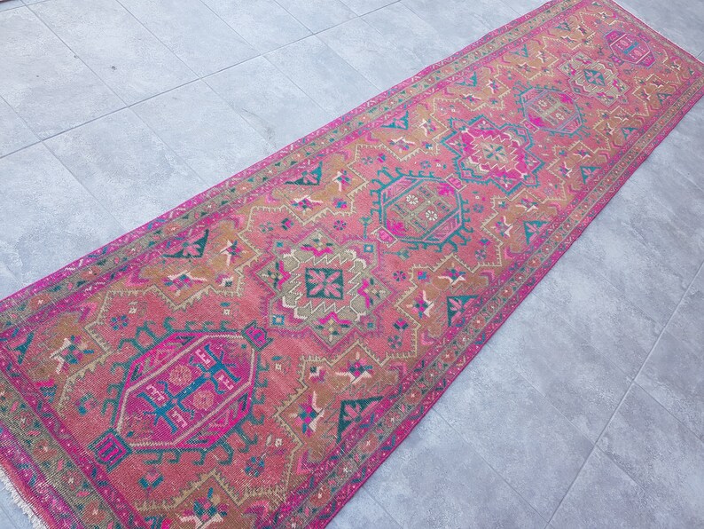 May include: A pink and brown patterned runner rug with intricate geometric designs. The rug has a fringed edge and is made of a soft, woven material.
