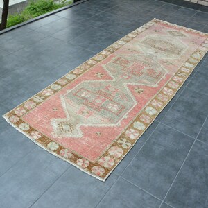 May include: A pink and beige runner rug with a traditional geometric pattern. The rug has a faded, vintage look and is perfect for adding a touch of bohemian style to any room.