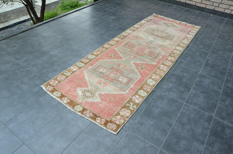 May include: A pink and beige runner rug with a traditional geometric pattern. The rug has a faded, vintage look and is perfect for adding a touch of bohemian style to any room.