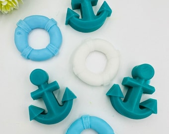 May include: An assortment of nautical-themed decorations, including teal anchors and light blue and white life preservers. These decorative items are arranged on a white surface, evoking a maritime theme.