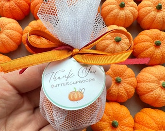 Könnte beinhalten: Ein kleiner weißer Tüllbeutel gefüllt mit Mini-Orangenkürbissen, gebunden mit einem rot-orangenen Band. Ein rundes Etikett mit dem Text "Thank You Buttercupgoods" und einer kleinen Kürbisillustration ist am Beutel befestigt.
