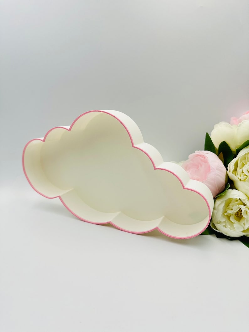 May include: White cloud-shaped box with a pink trim. The box is empty and is sitting on a white surface.