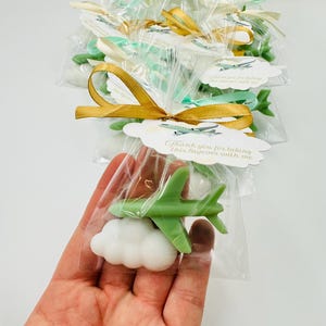 Peut inclure: Bonbons en forme d'avion vert et de nuage blanc dans des sachets en cellophane transparents, noués avec des rubans dorés et pastel. Chaque sachet porte une étiquette "Thank you for taking this layover with me."