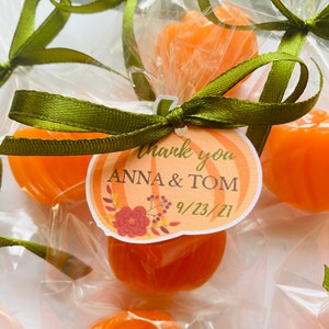 May include: Orange pumpkin-shaped candies wrapped in clear cellophane bags with green ribbon and a thank you tag that says "Thank you Anna & Tom 9/23/21".