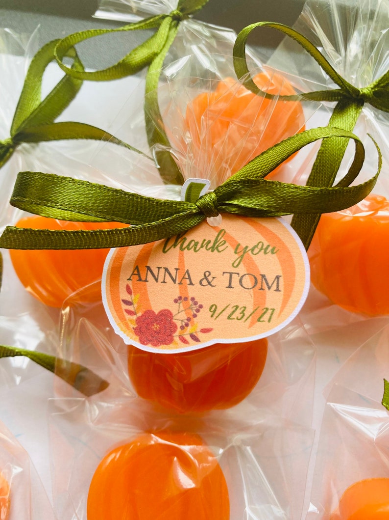 May include: Orange pumpkin-shaped candies wrapped in clear cellophane bags with green ribbon and a thank you tag that says "Thank you Anna & Tom 9/23/21".