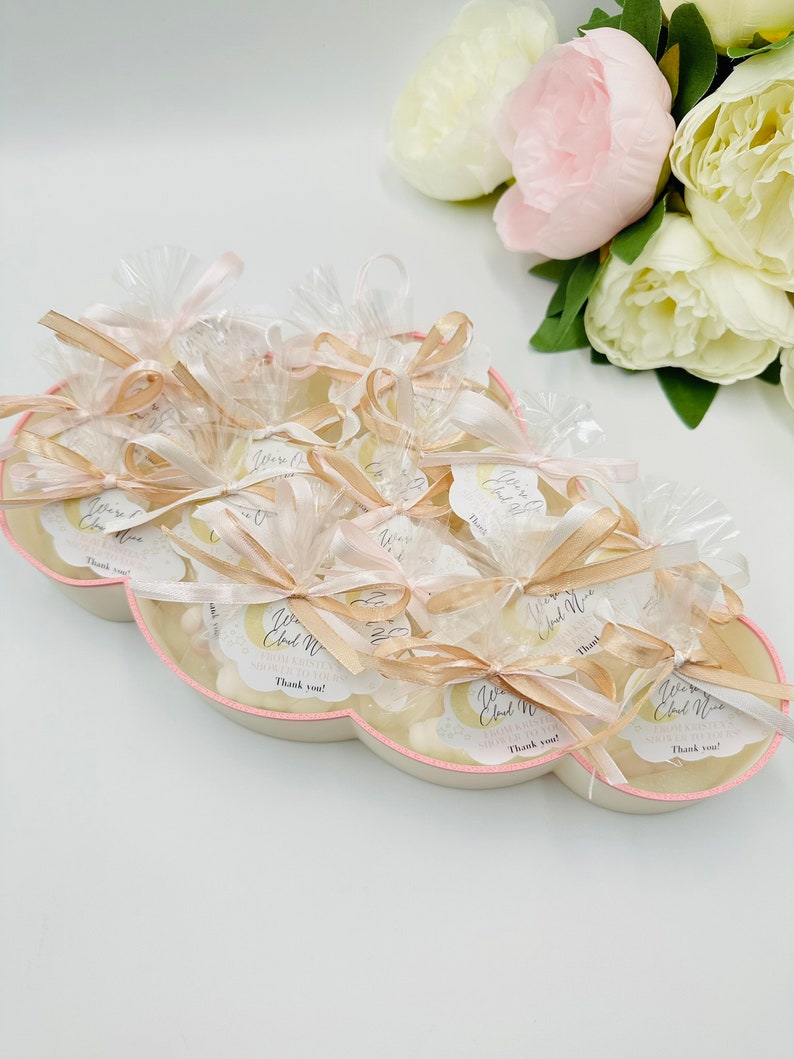 May include: A cloud-shaped tray filled with small white favors wrapped in clear cellophane bags tied with gold ribbon and a small tag that says "We're Having a Cloud Nine Baby Shower! Thank you!"