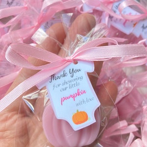 May include: Pink favor bags with a pink ribbon and a thank you tag that says "Thank You for showering our little pumpkin with love". The tag is shaped like a onesie with a pumpkin on it. The favor bags contain a pink pumpkin-shaped soap.