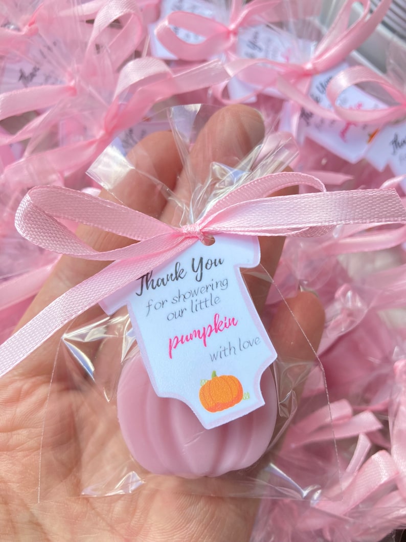 May include: Pink favor bags with a pink ribbon and a thank you tag that says "Thank You for showering our little pumpkin with love". The tag is shaped like a onesie with a pumpkin on it. The favor bags contain a pink pumpkin-shaped soap.