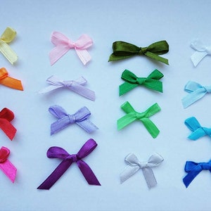 May include: Assortment of 16 small satin ribbon bows in various colors, including yellow, orange, pink, purple, green, blue, and white. The bows are arranged in rows on a white background.