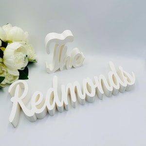 May include: White wooden sign with the words "The Redmonds" in a cursive font.