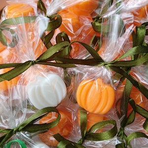 May include: A group of small, orange pumpkin-shaped soaps wrapped in clear cellophane bags and tied with green ribbon.