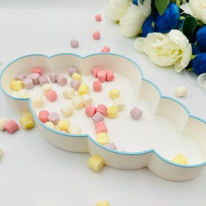 May include: A white cloud-shaped dish with a light blue rim filled with pastel-colored candy. The candy is scattered around the dish on a white surface.